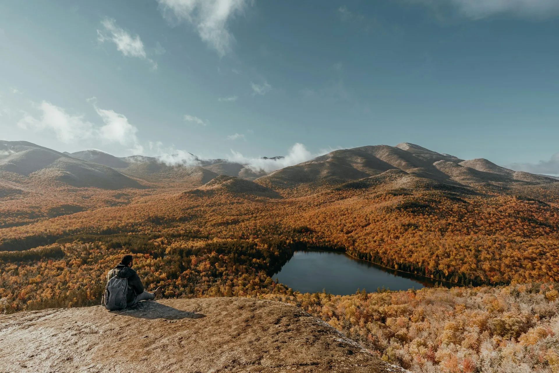 A hiker sitting on a rock above a lake and autumn hills